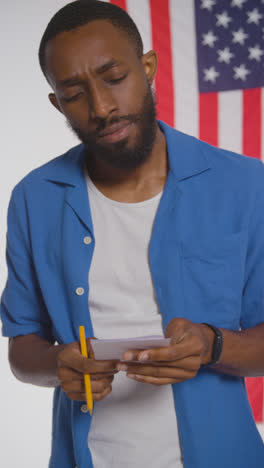 Vertical-Video-Shot-Of-Man-Next-To-Booth-With-Ballot-Paper-In-American-Election-Deciding-How-To-Cast-His-Vote-2